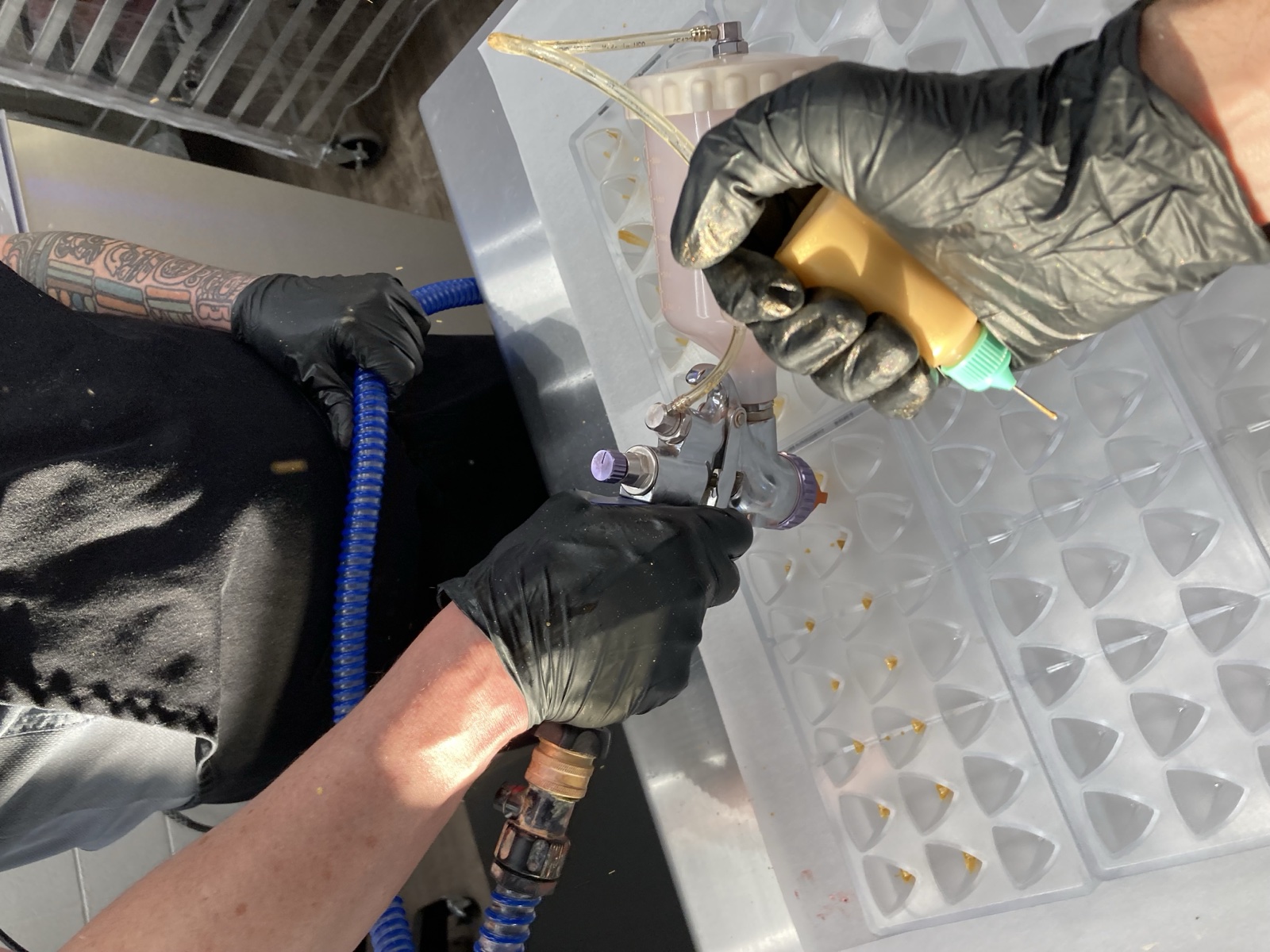 Gloved hands decorating chocolate moulds with a spray gun and fine detailing tool
